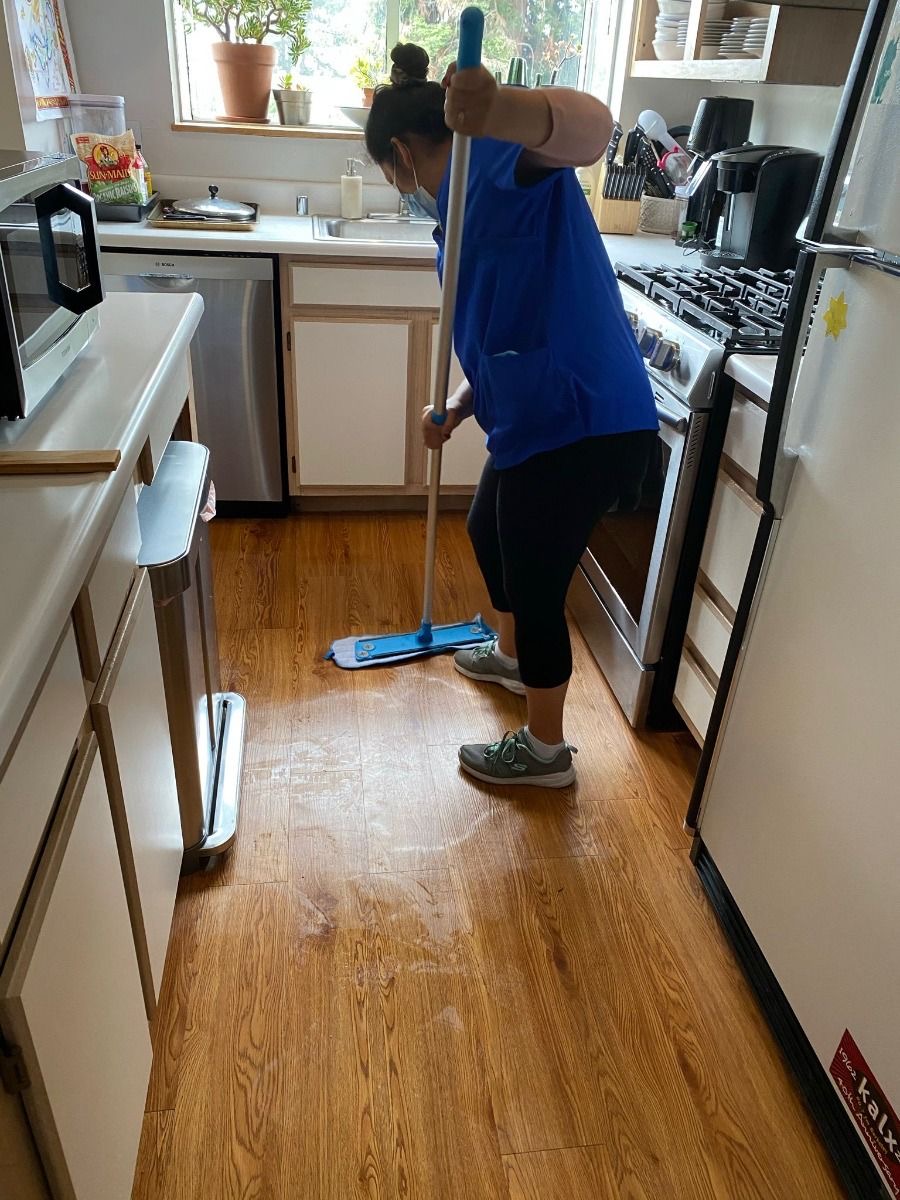Cleaner mopping a wood kitchen floor beside white cabinets