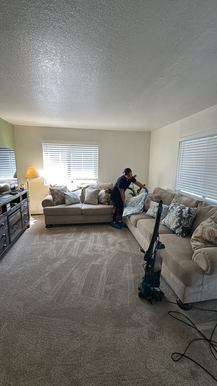 Cleaner tidying a beige sectional in a living room with fresh vacuum lines in the carpet